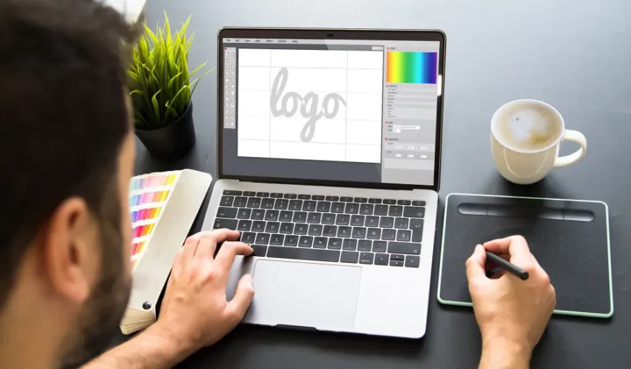 Die persönliche Anfrage Person entwirft ein Logo auf Laptop mit Kaffeetasse und Notizen auf dem Tisch.