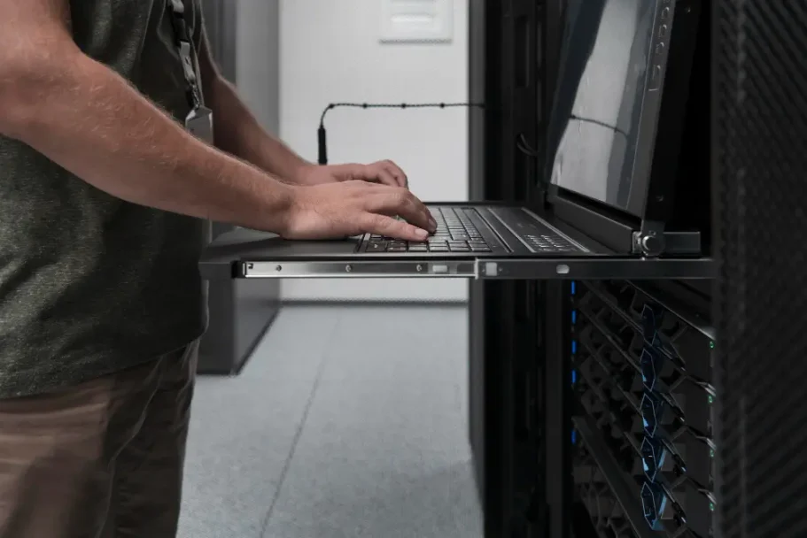 Überwachung Eine Person arbeitet an einem Laptop in einem Serverraum.
