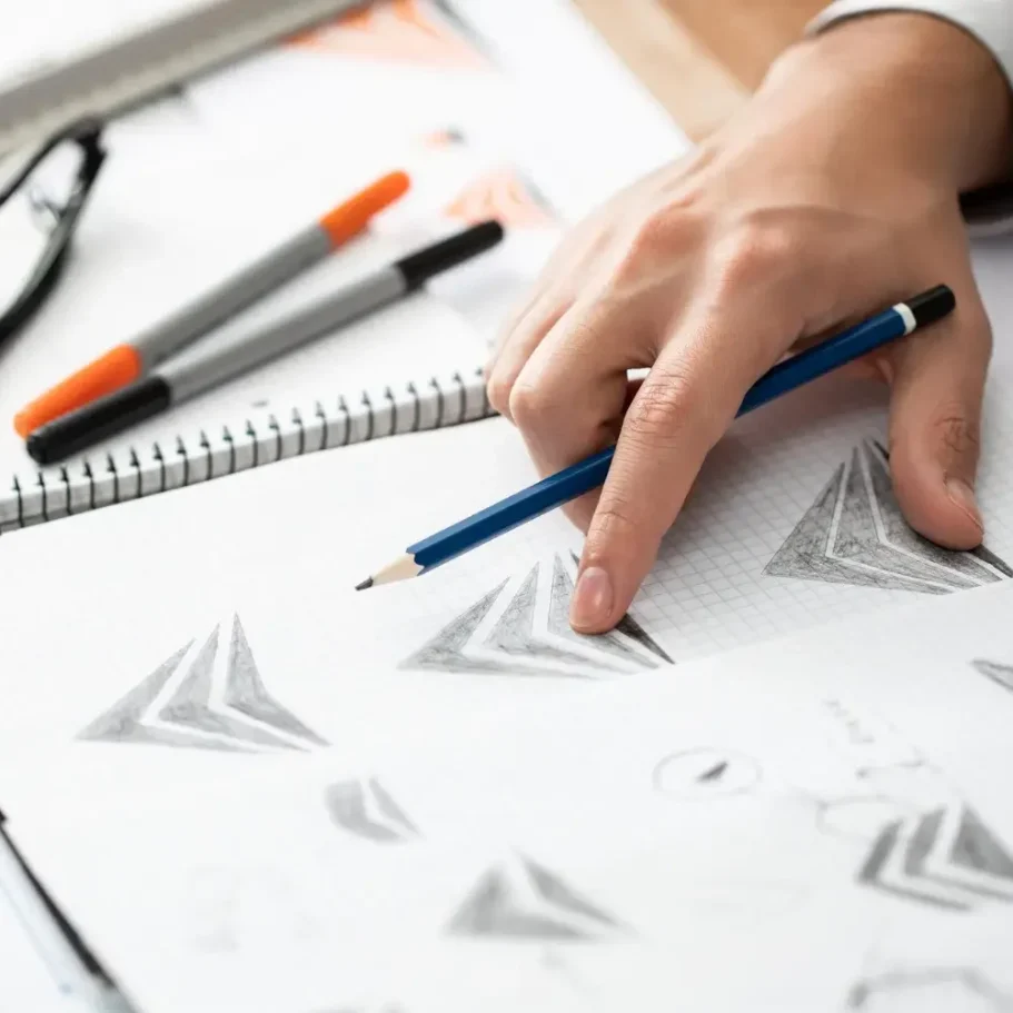 Eine Hand hält einen Bleistift über ein Skizzenblatt mit geometrischen Zeichnungen.