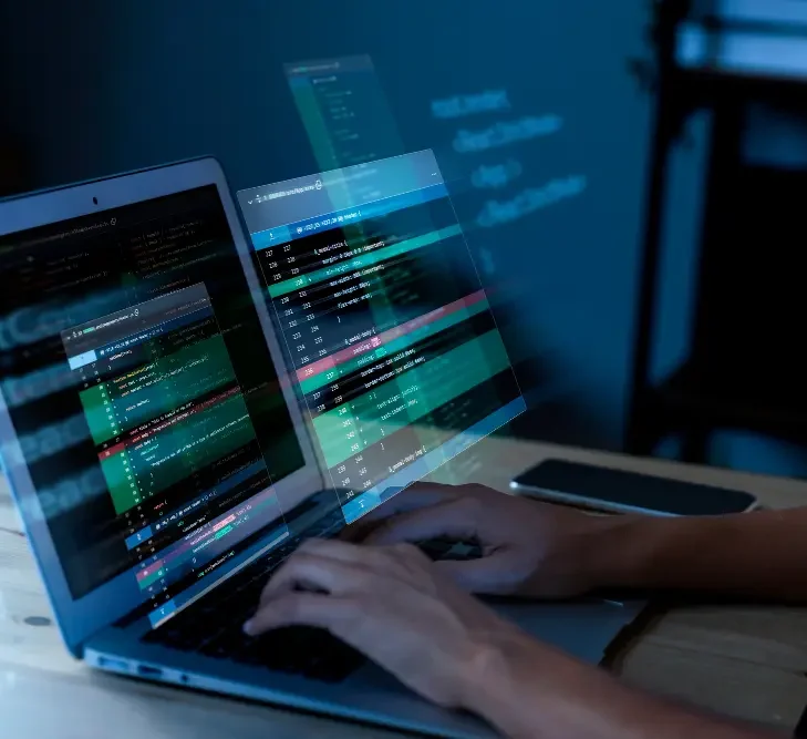 Eine Person tippt an einem Laptop, umgeben von Codezeilen auf einem Bildschirm.