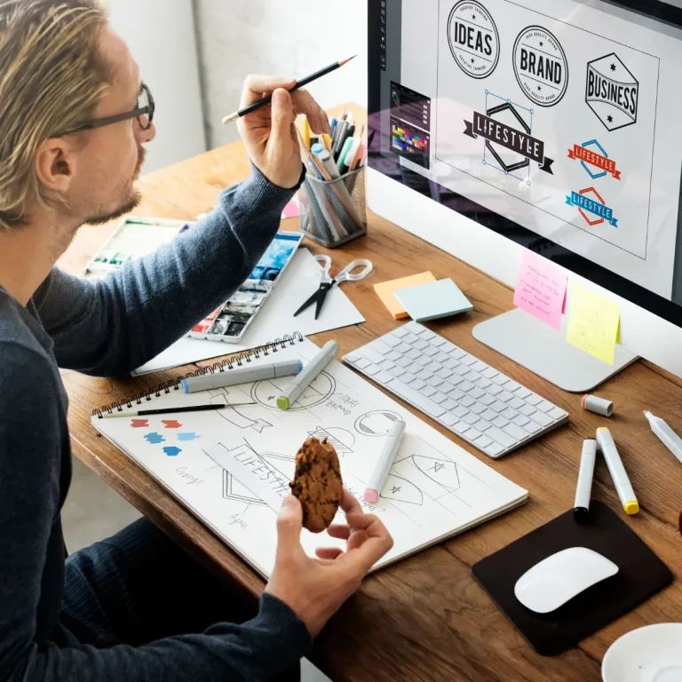 Ein Mann arbeitet an einem Computer, um Designs skizzieren, mit Zeichenmaterialien um ihn herum.