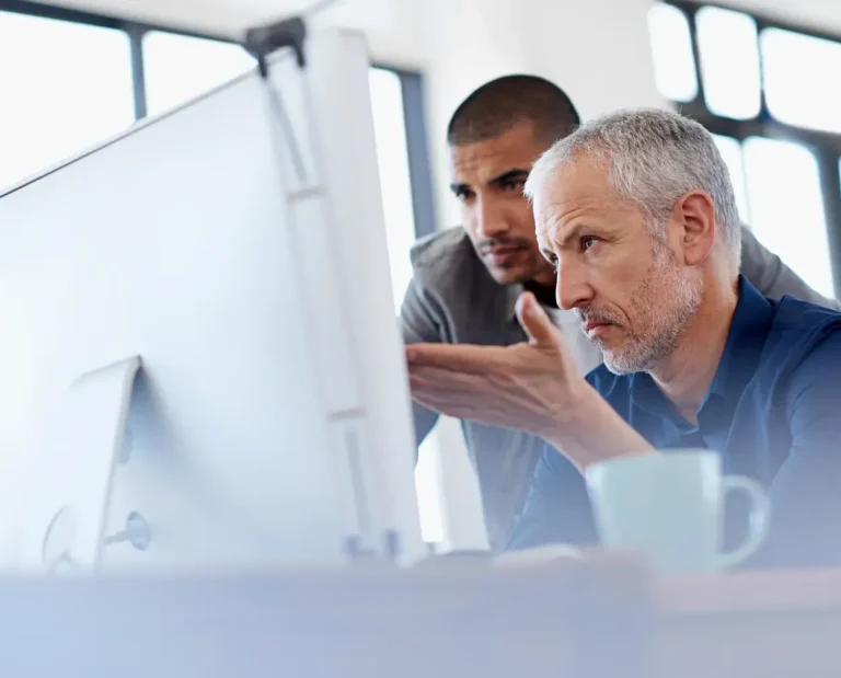Zwei Männer beobachten gemeinsam einen Computerbildschirm und diskutieren.
